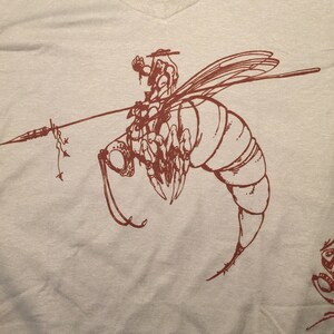 May include: A brown t-shirt with a graphic of a bee with a rider on its back. The bee is drawn in a detailed, stylized manner.