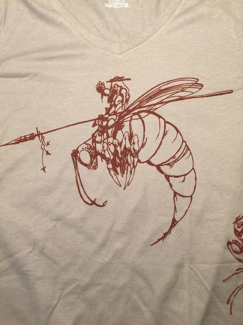 May include: A brown t-shirt with a graphic of a bee with a rider on its back. The bee is drawn in a detailed, stylized manner.