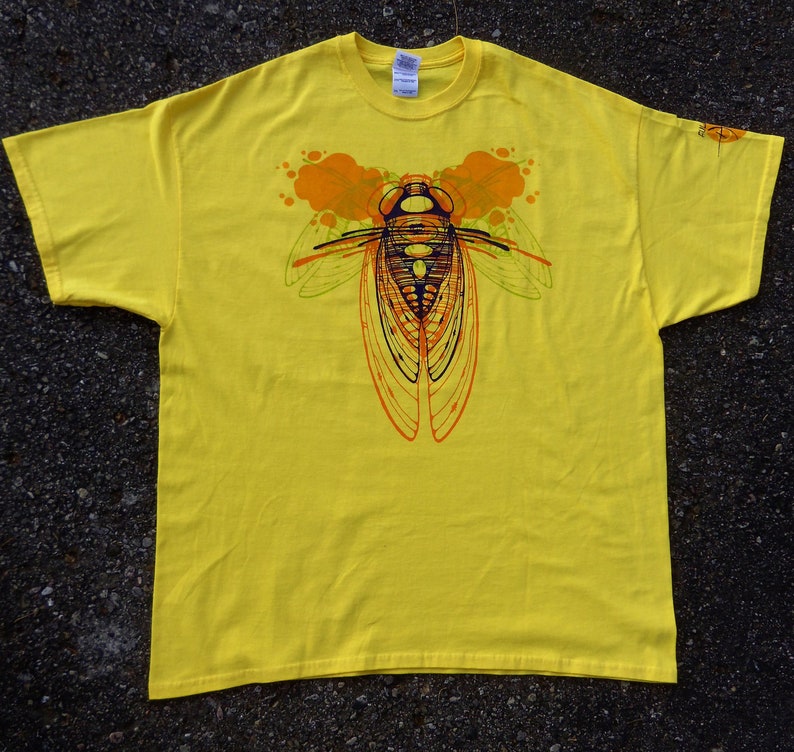 Pode incluir: Camiseta amarela com uma estampa gr&aacute;fica de um inseto cigarra com detalhes laranja e verde.