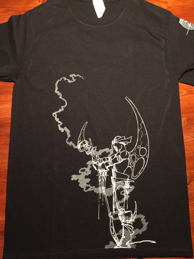 Op de afbeelding: Zwart T-shirt met een witte grafische print van een gestileerde figuur die een wapen vasthoudt en voor een rookwolk staat.