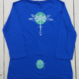 May include: A royal blue long-sleeved t-shirt with a white dragonfly graphic and a green circle. The text "Full Circle" is written in green on the bottom of the shirt.