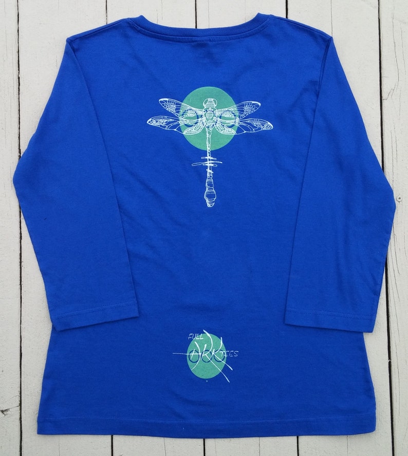 May include: A royal blue long-sleeved t-shirt with a white dragonfly graphic and a green circle. The text "Full Circle" is written in green on the bottom of the shirt.