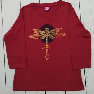 May include: A red long-sleeved shirt with a v-neck collar and a gold dragonfly graphic on the front.