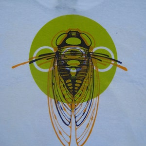 Pode incluir: Camiseta branca com um c&iacute;rculo verde e um gr&aacute;fico de cigarra preto e laranja.