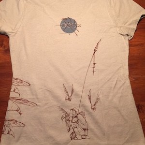 May include: A beige t-shirt with a brown graphic of a person fishing with a fishing rod and several insects flying around. The text "Full Circle" is printed on the back of the shirt.