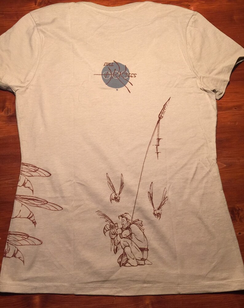 May include: A beige t-shirt with a brown graphic of a person fishing with a fishing rod and several insects flying around. The text "Full Circle" is printed on the back of the shirt.