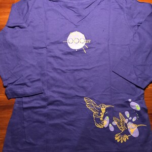 K&ouml;nnte beinhalten: Lilafarbenes Langarmshirt mit einem gelben Kolibri-Design und dem Text "Ooozes" auf der R&uuml;ckseite.