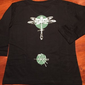 May include: Black long-sleeved shirt with a green circle and a white dragonfly graphic on the back. The text "Full Dark Trees" is printed below the dragonfly.