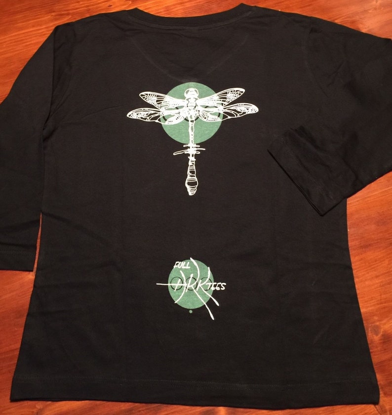 May include: Black long-sleeved shirt with a green circle and a white dragonfly graphic on the back. The text "Full Dark Trees" is printed below the dragonfly.