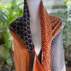 May include: A multi-colored scarf with a geometric pattern in shades of brown, orange, and white. The scarf is made of a soft, lightweight fabric and is perfect for adding a touch of style to any outfit.