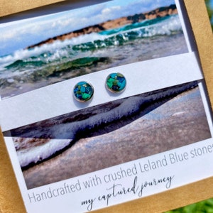 May include: A pair of silver stud earrings with blue and green crushed Leland Blue stones. The earrings are handcrafted and feature the text "my captured journey".