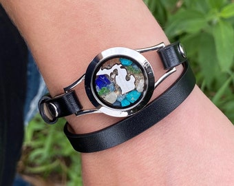 Könnte beinhalten: Ein schwarzes Lederarmband mit einem silbernen Anhänger, der einen Bundesstaat-Umriss zeigt, der mit buntem Sand und Steinen gefüllt ist.