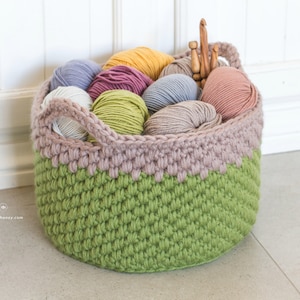 May include: A green and pink crocheted basket filled with colorful yarn balls and knitting needles.
