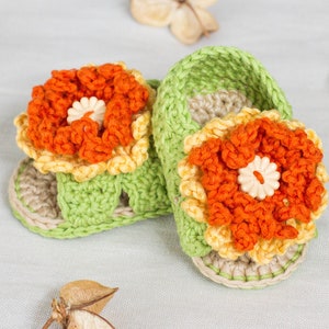 May include: A pair of green crocheted baby sandals with orange and yellow flower embellishments.