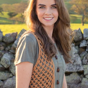 Peut inclure: Une femme portant un gilet en crochet marron sur un t-shirt vert. Le gilet a un motif g&eacute;om&eacute;trique et la femme porte un collier avec des perles en bois.