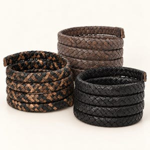 May include: Three coiled bracelets featuring a braided texture. One bracelet is solid black, one is solid brown, and one is a mix of black and brown woven strands. Each bracelet is formed into a multi-layered spiral shape with visible ends.