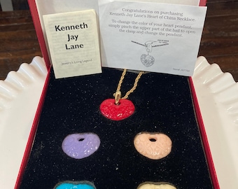 Peut inclure: Un ensemble de collier Kenneth Jay Lane Heart of China dans une boîte rouge. L'ensemble comprend un collier chaîne dorée avec un pendentif cœur rouge et quatre pendentifs en forme de cœur supplémentaires en violet, pêche, turquoise et crème. La boîte contient une carte avec des instructions.