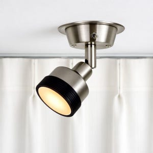 Könnte beinhalten: Ein Deckenstrahler aus gebürstetem Nickel. Das Licht hat einen zylindrischen Kopf mit einem schwarzen Gummiring um die Lichtöffnung. Die Leuchte ist an einer weißen Decke montiert. Das Licht ist eingeschaltet und strahlt ein warmes Leuchten aus.