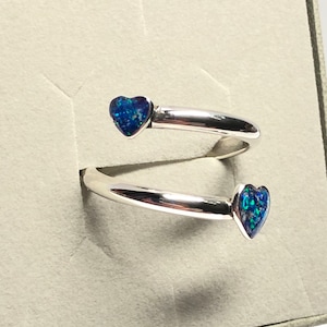 Könnte beinhalten: Ein silberner Ring mit zwei herzförmigen Steinen aus blauem Opal. Der Ring ist ein doppelter Band, der sich um den Finger dreht.