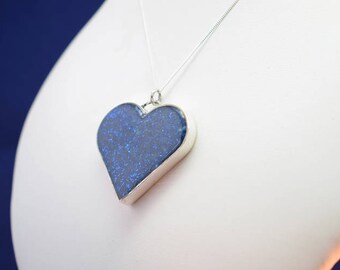 May include: A silver chain necklace with a blue heart-shaped pendant. The pendant has a sparkly, glittery finish.