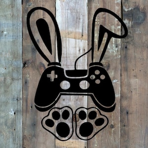 May include: Black graphic of a video game controller with bunny ears and paw prints. The controller has a plus sign and circle, square, and X buttons. The image is on a wooden background.