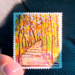 May include: A rectangular postage stamp featuring a watercolor illustration of a path winding through a forest with vibrant yellow and orange autumn leaves on the trees and a light-colored ground, finished with a classic perforated edge border.