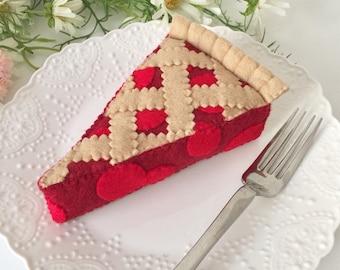 Puede incluir: Una rebanada de pastel de cereza de fieltro con un relleno rojo y una corteza tostada. La rebanada de pastel está en un plato blanco con un tenedor plateado.