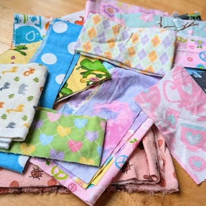 May include: A collection of colorful fabric scraps with various patterns, including animals, hearts, and peace signs. The fabrics are in shades of pink, blue, green, yellow, and white.