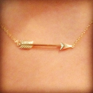 May include: A gold arrow necklace with a delicate chain. The arrow pendant is simple and elegant.