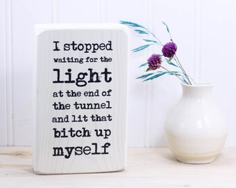 Small whitewashed wood sign with motivational quote, "I stopped waiting for the light at the end of the tunnel and lit that b*tch up myself"