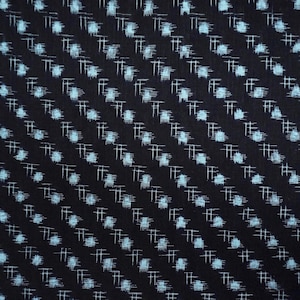 May include: Close-up of a dark blue fabric featuring a repeating pattern of light blue dots and white cross-like shapes arranged diagonally. The fabric appears textured, possibly woven.
