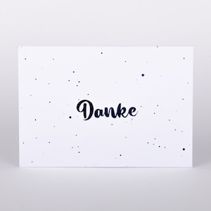 Könnte beinhalten: Eine weiße Karte mit einem blau gesprenkelten Hintergrund und dem Wort "Danke" in schwarzer Schrift.