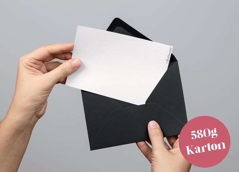 May include: A white card is being removed from a black envelope. The card has text in the upper right corner. A pink circle with the text "580g Karton" is in the lower right corner.