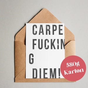 Op de afbeelding: Een witte kaart met de tekst "CARPE FUCKING DIEM!" in een vetgedrukte, zwarte letter, in een bruine envelop. Een rode cirkel met de tekst "580g Karton" staat in de rechter benedenhoek. De achtergrond is lichtgrijs.