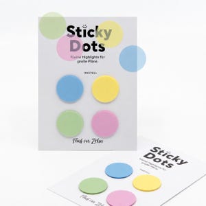 May include: Two white rectangular cards featuring the text Sticky Dots and Kleine Highlights für große Pläne. Each card displays four circular adhesive stickers in pastel blue, yellow, green, and pink, arranged in a two-by-two grid pattern.
