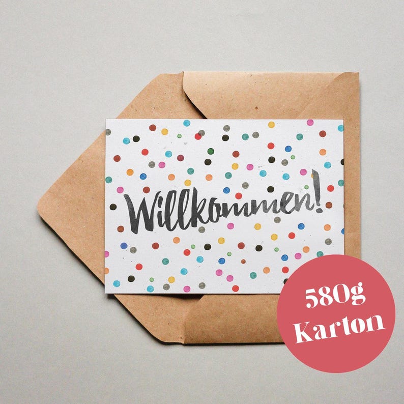 Puede incluir: Una tarjeta blanca con un patr&oacute;n de confeti de colores y la palabra "Willkommen!" en escritura negra. La tarjeta est&aacute; en un sobre marr&oacute;n. El texto "580g Karton" est&aacute; impreso en un c&iacute;rculo rojo.
