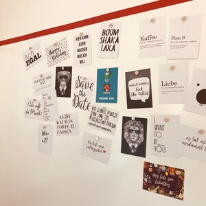 Puede incluir: Una pared blanca con una franja roja en la parte superior. Hay muchas tarjetas peque&ntilde;as clavadas en la pared con varios textos e im&aacute;genes. Algunos de los textos incluyen "Save the Date", "Boom Shaka Laka", "Ach Egal", "Kaffee", "Plan B", "Liebe", "Indlich Sommer, Fuck The Pallis!" y "es tut mir so verdammt Leid".