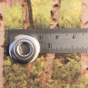 May include: A silver metal washer with a hole in the center. The washer is about 1 inch in diameter.