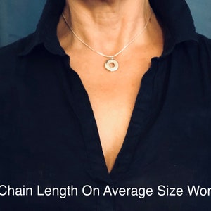May include: A silver chain necklace with a circular pendant, shown on a person wearing a black shirt. The chain is 16 inches long.  "16" Chain Length On Average Size Woman"