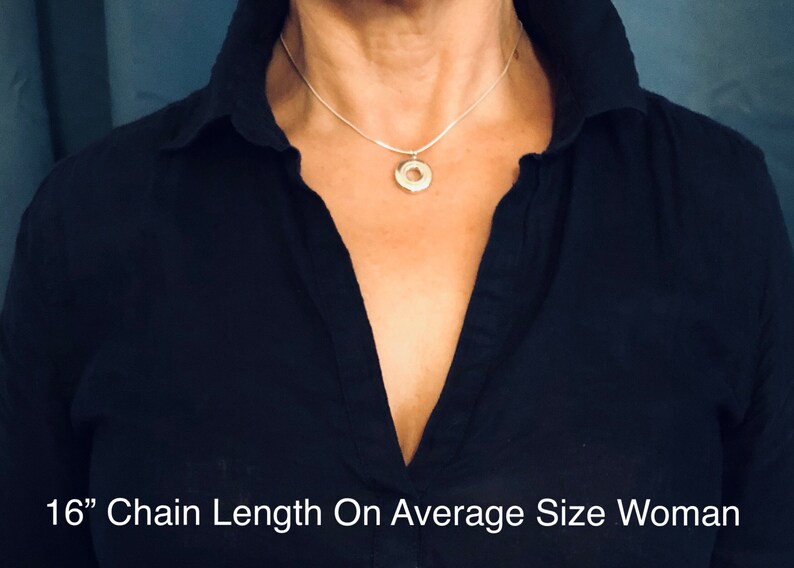 May include: A silver chain necklace with a circular pendant, shown on a person wearing a black shirt. The chain is 16 inches long.  "16" Chain Length On Average Size Woman"