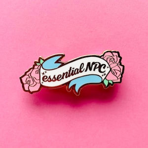 May include: Gold-tone enamel pin with a white banner that reads "essential NPC" in brown lettering. The banner is decorated with two pink roses and a blue ribbon.