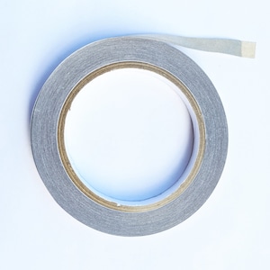 May include: A roll of silver-coloured tape with a white backing. The tape is partially unwound, showing the adhesive side.