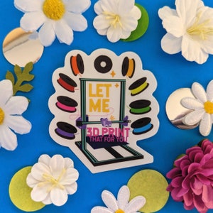 Peut inclure: Un autocollant blanc avec un design d'imprimante 3D et le texte "Let Me 3D Print That For You". L'autocollant est entouré de bobines de filament colorées.