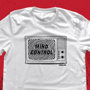 May include: White t-shirt with a black and white illustration of a vintage television with the text "MIND CONTROL" on the screen. The text "OBELISK" is below the television.