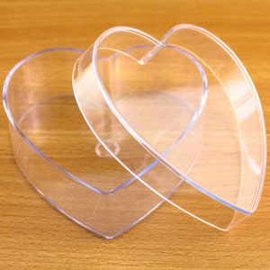 May include: A clear plastic heart-shaped box with a lid. The box is open and the lid is resting on top of the box.