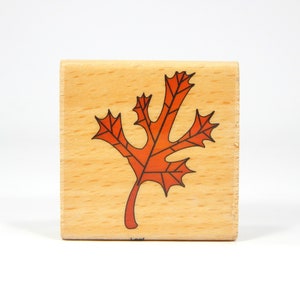 May include: A wooden stamp with a red and black leaf design. The stamp is rectangular and has the word "Leaf" printed on the bottom.