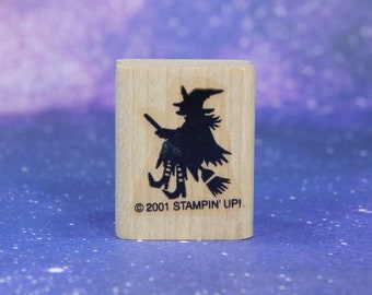 Könnte beinhalten: Ein Holzstempel mit einer schwarzen Silhouette einer Hexe auf einem Besen. Die Hexe trägt einen spitzen Hut und fliegt nach links. Der Stempel trägt den Text "© 2001 STAMPIN' UP!" am unteren Rand.