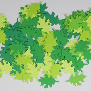 May include: A collection of green and yellow paper leaves, scattered on a white background. The leaves are cut in the shape of maple leaves.