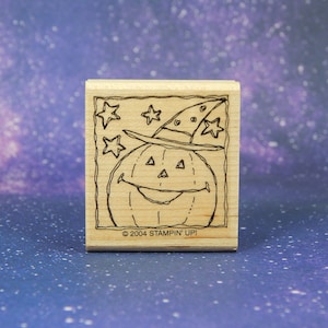 May include: Wooden stamp featuring a smiling jack-o'-lantern wearing a witch's hat, surrounded by stars. The stamp is a square shape with the text "© 2004 STAMPIN' UP!" at the bottom. Perfect for Halloween crafts.