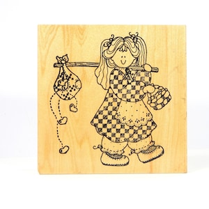 May include: A wooden stamp with a black and white illustration of a girl carrying a bag of hearts. The girl is wearing a checkered dress and has pigtails.